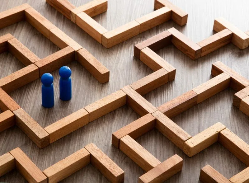 Zwei blaue Spielfiguren stehen am Eingang eines Labyrinths aus Holzklötzen.